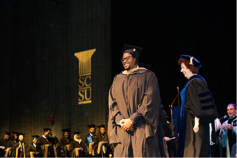 A student in cap and gown at the podium during graduation ceremony