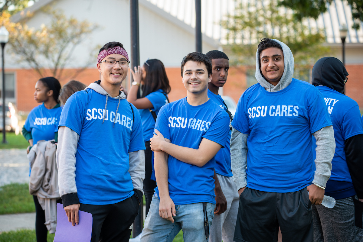 Three volunteers wearing Serving the Community shirt