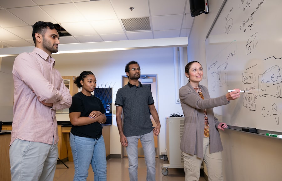 Professor writing on a whiteboard with students watching