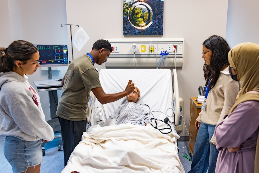 Students training to be a nurse, a male student holds a bottle for a dummy patient